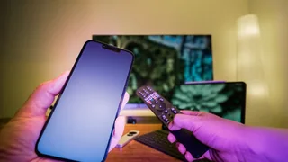 Telemóvel em primeiro plano junto a um televisor e um comando.